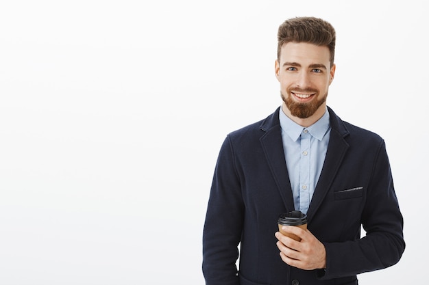 Al dinero le gusta la confianza. Hombre guapo carismático e inteligente seguro de sí mismo con cabello castaño, barba y ojos azules sosteniendo una taza de café de papel sonriendo felizmente conociendo a una linda chica después del trabajo en la cafetería