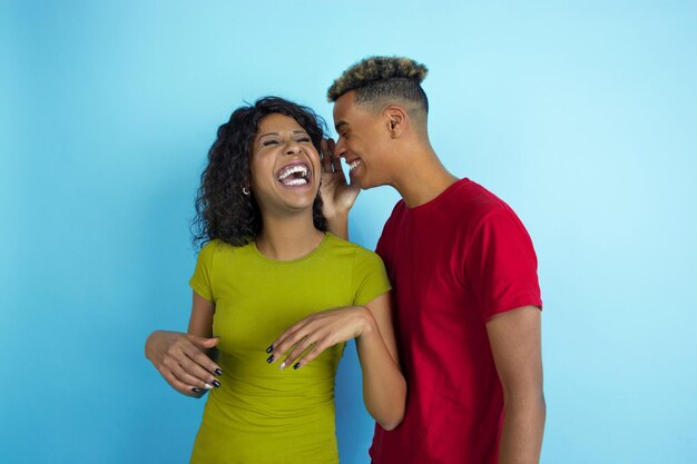 Al escuchar el secreto, se ríe. Joven emocional afroamericano y mujer en ropa colorida sobre fondo azul.