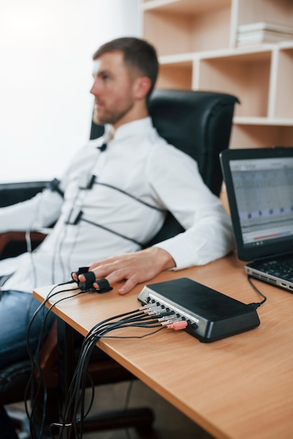 Foto gratuita al joven empresario no le gustan sus empleados. hoy sabremos si eso es cierto. hombre sospechoso pasa el detector de mentiras en la oficina. haciendo preguntas