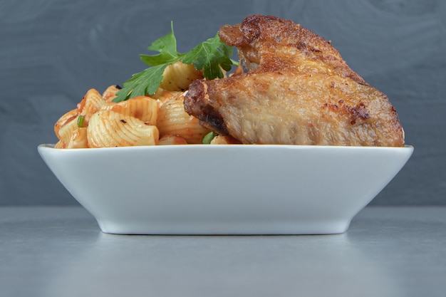 Alas fritas y pasta de conchas en un tazón blanco.