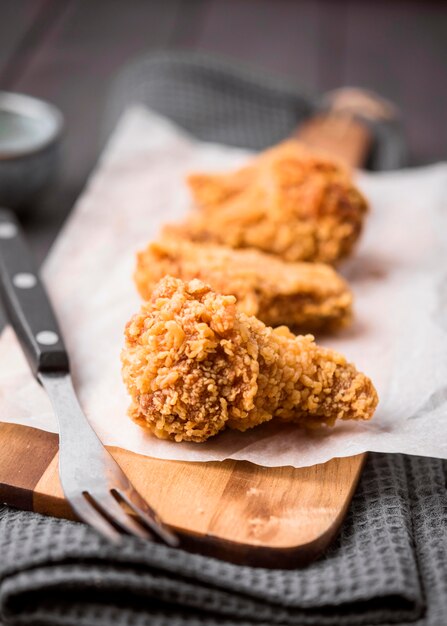 Alas de pollo frito de primer plano en la tabla de cortar con un tenedor