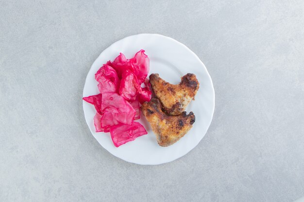 Alas de pollo a la parrilla y repollo en un plato blanco.