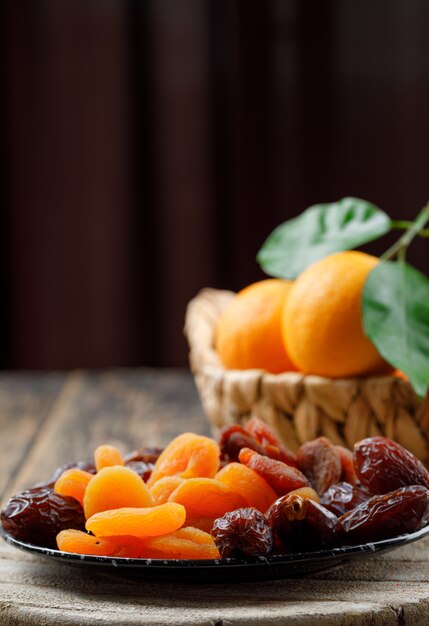 Albaricoques secos en un plato con fechas y naranjas en la cesta