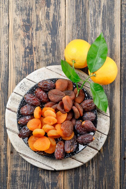 Albaricoques secos en un plato con fechas y naranjas vista superior en madera y tabla de cortar