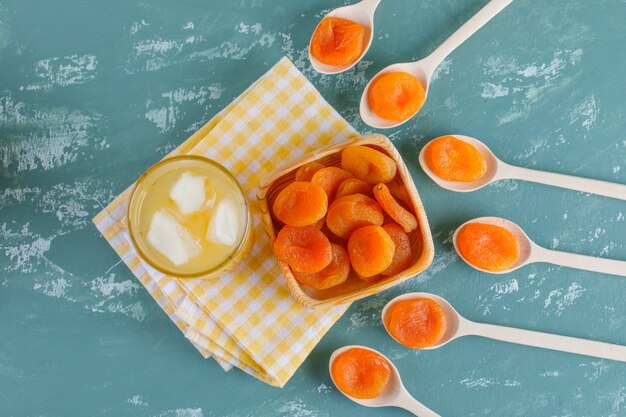 Albaricoques secos en plato de madera y cucharas con vista superior de jugo en yeso y tela de picnic