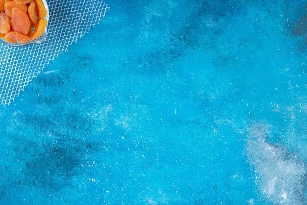 Albaricoques secos en un recipiente de vidrio, sobre la mesa azul.