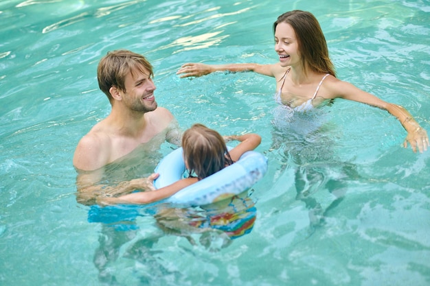 En la alberca. Padres enseñando a su hija a nadar y luciendo involucrados