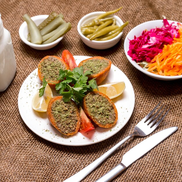 Albóndigas rellenas turcas ichli kofte servidas con tomate limón, perejil y pepinillos