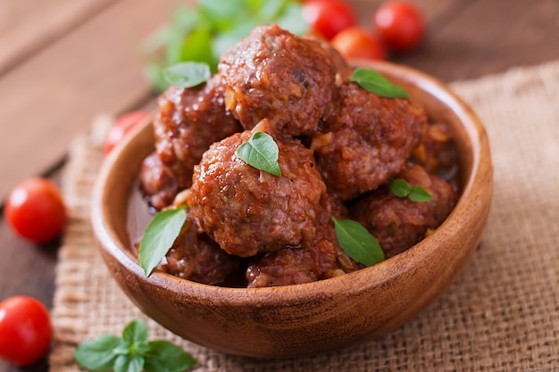 Albóndigas en salsa de tomate agridulce y albahaca en un tazón de madera