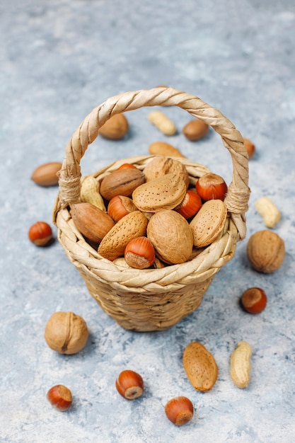 Alcance de la cesta en varios tipos de nueces en cáscaras, cacahuetes, almendras, avellanas y nueces sobre superficie de concreto