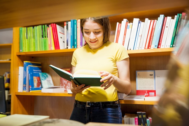 Alegre adolescente leyendo detrás de librería