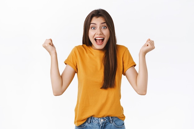 Alegre, afortunada, aliviada, atractiva mujer ganadora del premio, bomba de puño, triunfando alegremente, gritando de felicidad, regocijándose, apoyando al equipo viendo un juego emocionante, de pie, fondo blanco.