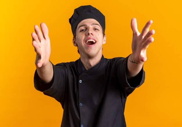 Foto gratuita alegre y amable joven cocinero de sexo masculino rubio en uniforme de chef y gorra haciendo gesto de bienvenida