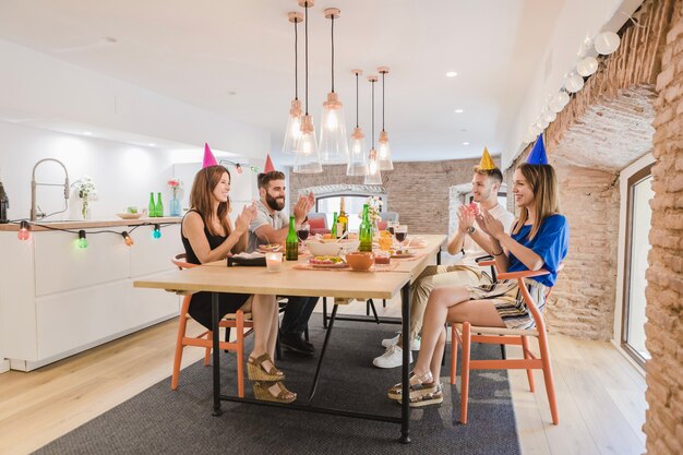 Alegre amigos sentado a la mesa y aplaudiendo