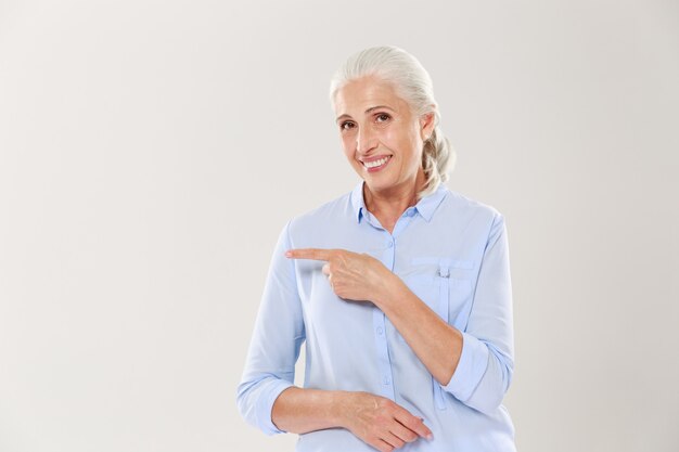 Alegre anciana en camisa azul, señalando con el dedo en el copyspace vacío