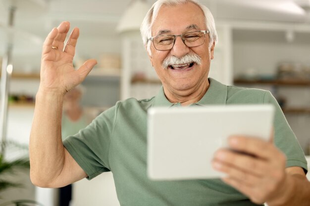 Alegre anciano divirtiéndose mientras usa el panel táctil en casa