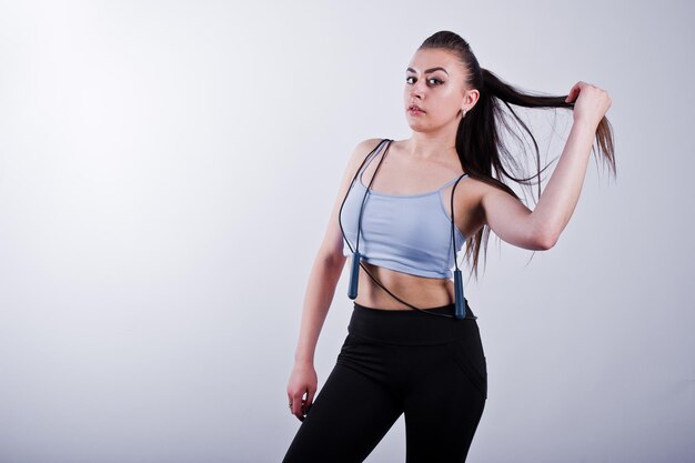 Alegre y atractiva mujer joven en fitness con top y polainas negras con cuerda para saltar aislada sobre fondo blanco