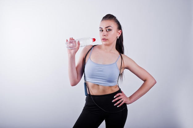 Alegre y atractiva mujer joven en fitness con top y polainas negras con cuerda para saltar y una botella de agua aislada sobre fondo blanco