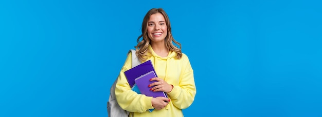 Foto gratuita alegre bonita chica rubia sonriendo a la cámara llevar mochila y cuadernos papeles para estudiar learni