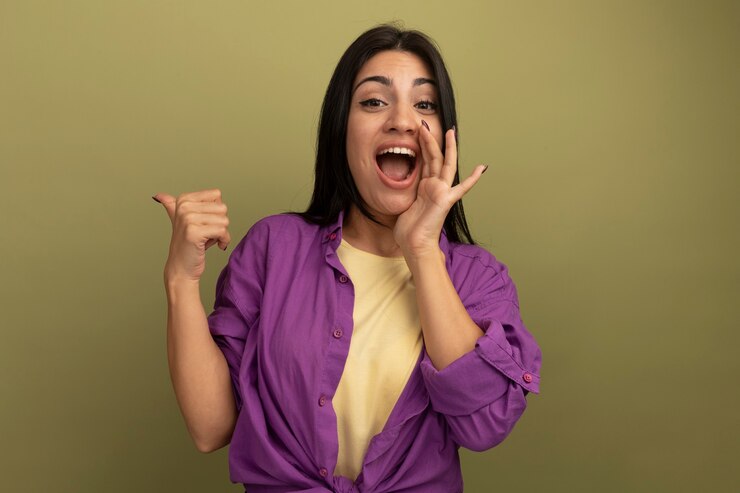 Foto gratuito alegre bonita morena chica caucásica sostiene la mano cerca de la boca y apunta hacia atrás en verde oliva