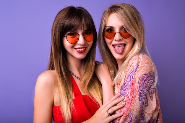 Alegre brillante retrato positivo de la hermana bonita de la mujer mejores amigos posando en el espacio violeta, mostrando lengua y sonrisa, abrazos y familia,