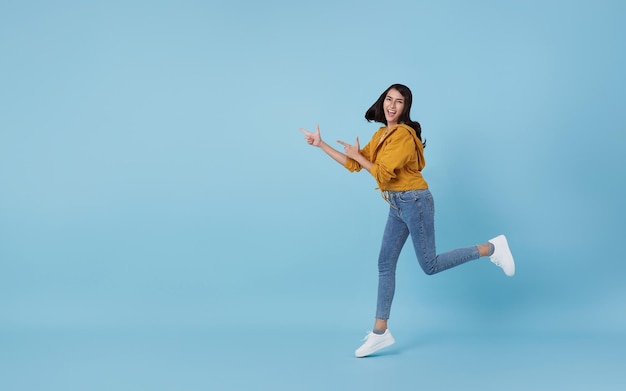 Alegre chica asiática saltando en el aire señalando con el dedo para copiar el espacio con cara sonriente y feliz