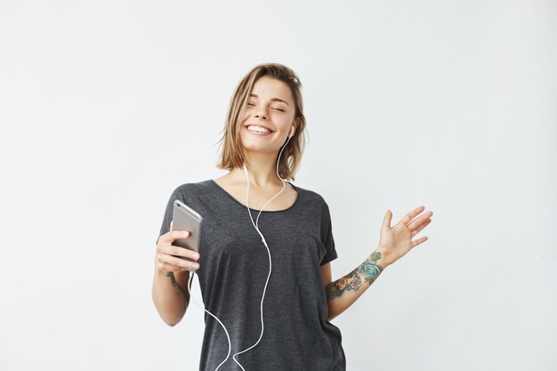 Alegre chica guapa joven sonriente escuchando música en auriculares bailando. Ojos cerrados.