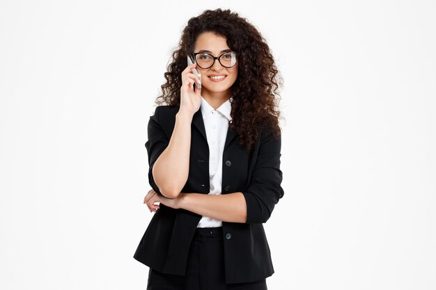 alegre chica de negocios rizada con gafas hablando por teléfono