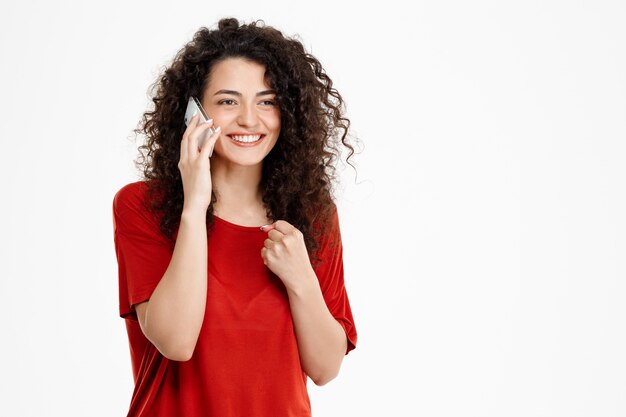 alegre chica rizada hablando por su teléfono