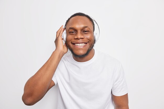 Alegre chico afroamericano escucha su música favorita a través de auriculares sonríe alegremente