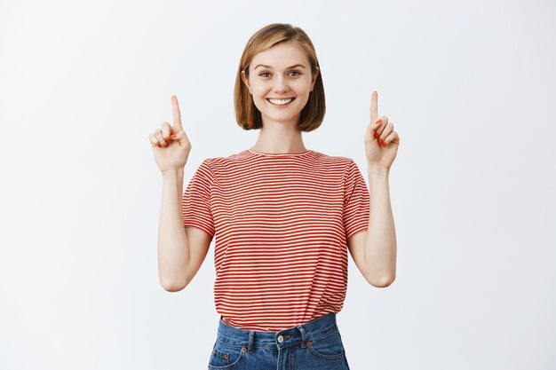 Alegre, confiada mujer bonita apuntando con el dedo hacia arriba y sonriendo feliz