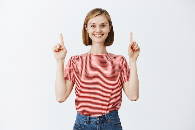 Alegre, confiada mujer bonita apuntando con el dedo hacia arriba y sonriendo feliz