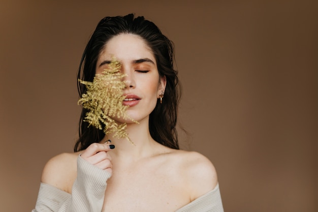 Alegre dama europea con maquillaje nude posando con planta. Glamorosa modelo femenina morena escalofriante.