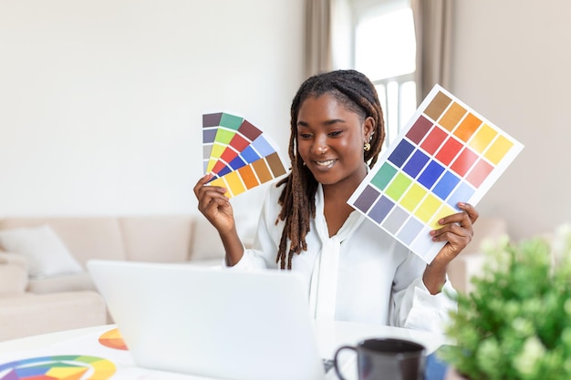 Alegre diseñadora afroamericana teniendo videoconferencia con clientes sentados en el escritorio frente a la computadora sosteniendo paletas de colores gesticulando y sonriendo espacio de copia
