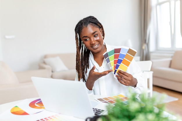 Alegre diseñadora afroamericana teniendo videoconferencia con clientes sentados en el escritorio frente a la computadora sosteniendo paletas de colores gesticulando y sonriendo espacio de copia