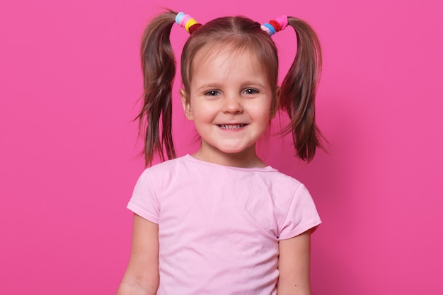 alegre y dulce niña con coletas graciosas, sonriendo sinceramente, de pie, erguidos y coloridos. Copiar espacio para publicidad.