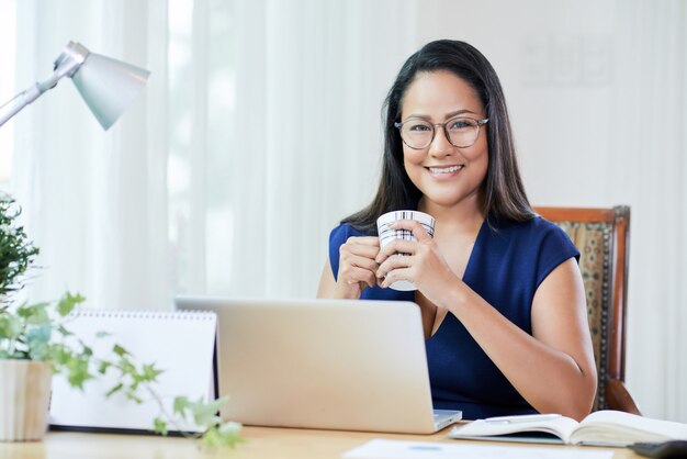 Alegre empresaria con café en el escritorio de trabajo