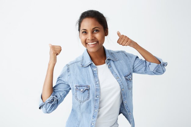 Alegre entusiasta hermosa mujer afroamericana con cabello negro mostrando pulgares arriba gesto, expresión de su agrado y aprobación de idea o proyecto, sonriendo ampliamente.