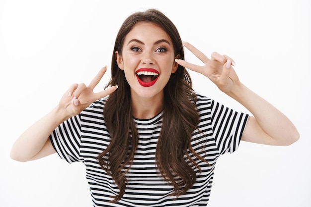 Alegre y entusiasta mujer feliz con lápiz labial rojo, camiseta a rayas, divirtiéndose, disfrutando de un impresionante viaje turístico, mostrar la paz, el signo de la victoria posando con alegría