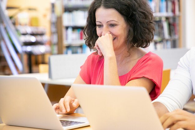 Alegre estudiante adulto disfrutando de contenido en computadora