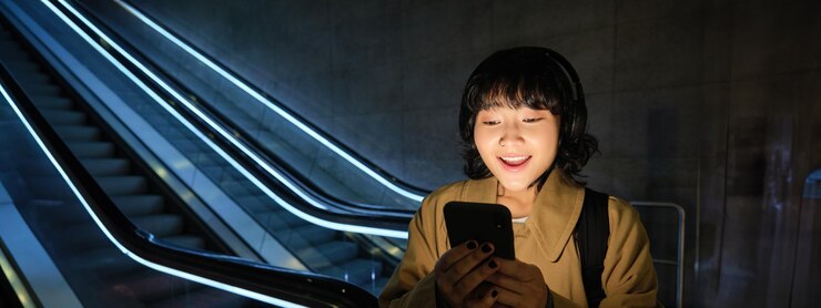Foto gratuito alegre estudiante asiática que parece sorprendida y feliz en la pantalla del teléfono inteligente leyendo noticias increíbles