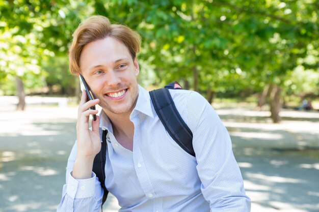 Alegre estudiante feliz con mochila hablando por teléfono