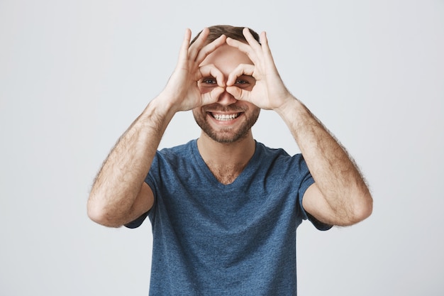 Alegre guapo sonriente muestra signos bien sobre los ojos