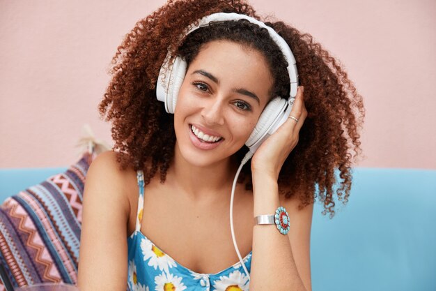 Alegre hermosa mujer de piel oscura usa grandes auriculares modernos, escucha música agradable mientras descansa en casa durante el día libre en la universidad o el trabajo.