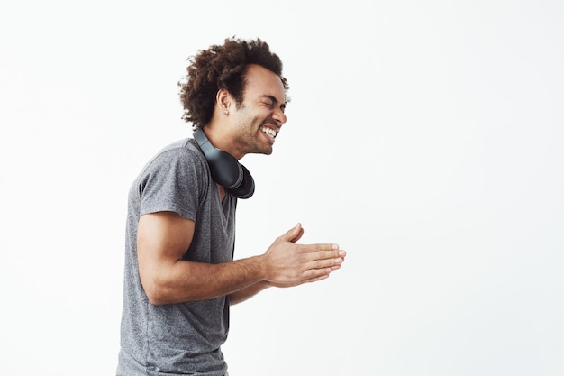 Alegre hombre africano con auriculares riendo de pie en el perfil