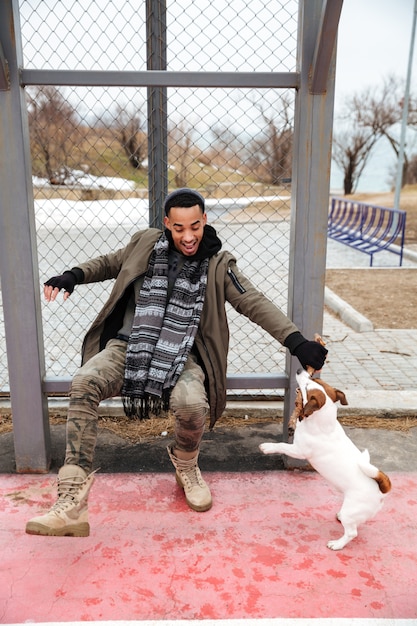 Foto gratuita alegre hombre africano jugando con perro y riendo al aire libre