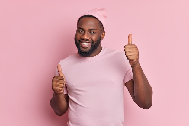 Alegre hombre afroamericano de piel oscura baila despreocupado mantiene los pulgares hacia arriba tiene una sonrisa brillante demuestra que le gusta algo