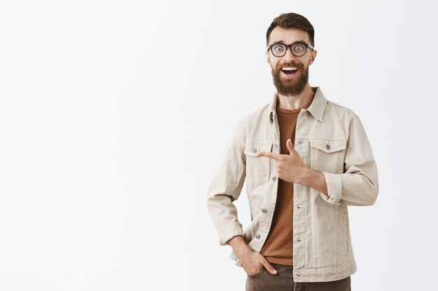 Alegre hombre barbudo con barba en gafas posando contra la pared blanca