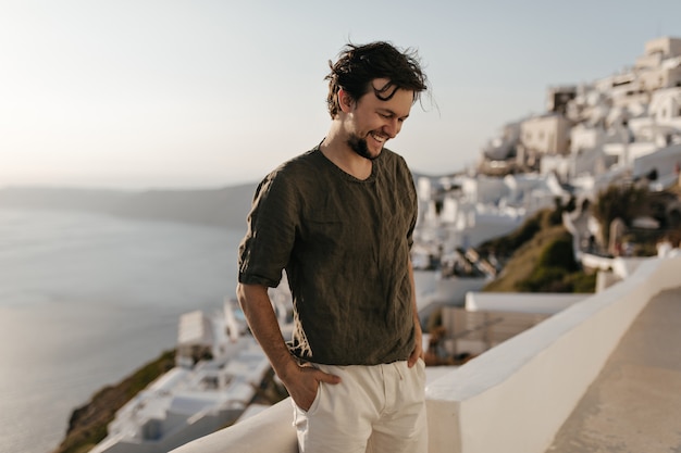 Alegre hombre morena feliz en camiseta verde oscuro y pantalones cortos blancos sonríe sinceramente afuera