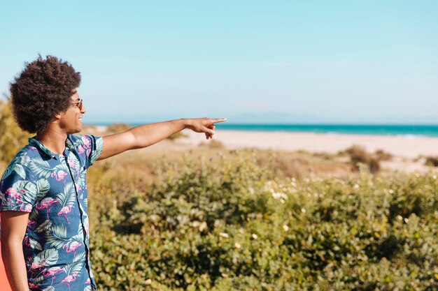 Alegre hombre negro joven apuntando dirección en la playa